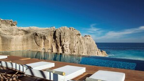 Zona junto a la piscina con sillones de descanso, vista despejada del océano y acantilados rocosos al fondo.