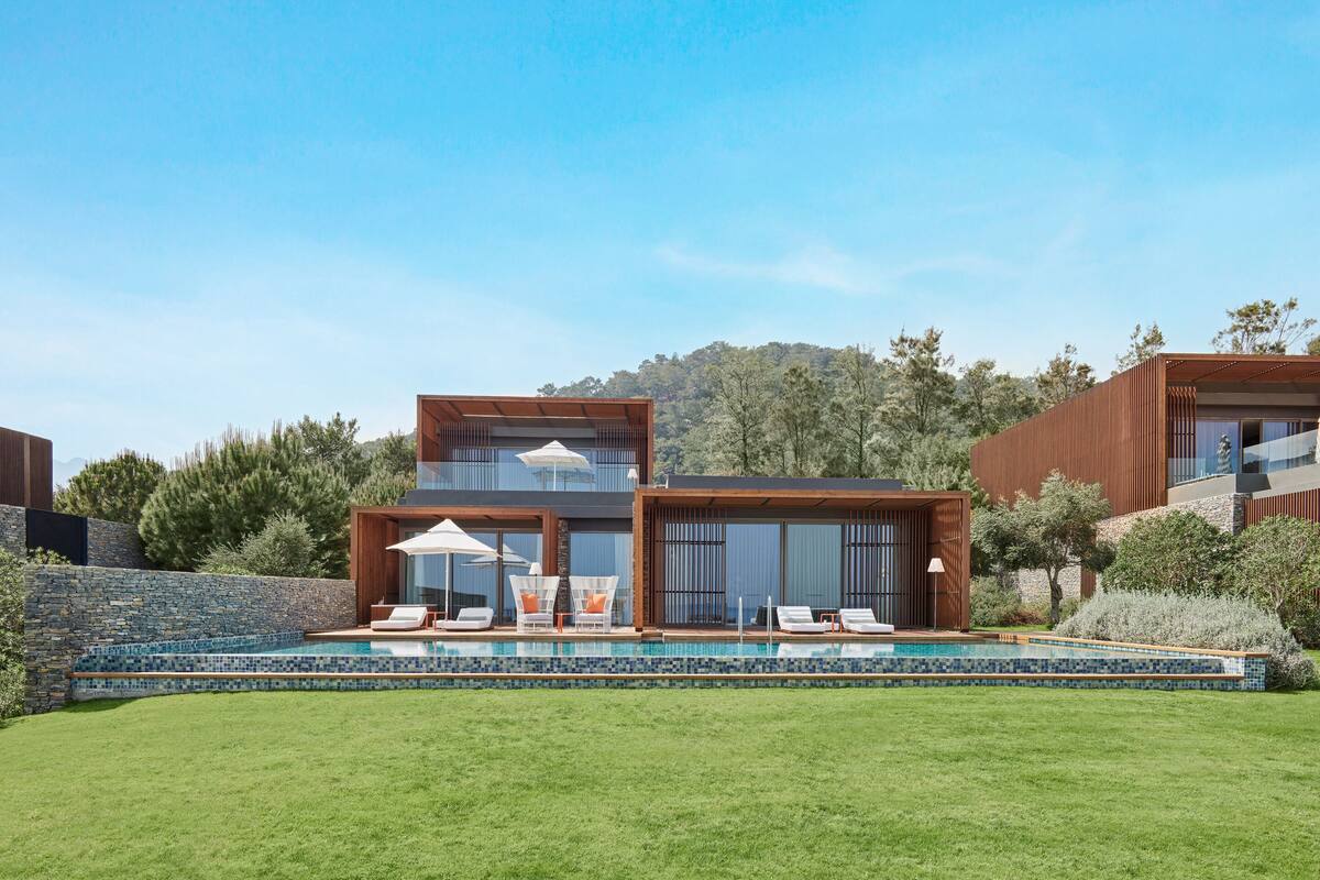 A modern two-story house with a swimming pool, outdoor seating, and a stone wall.