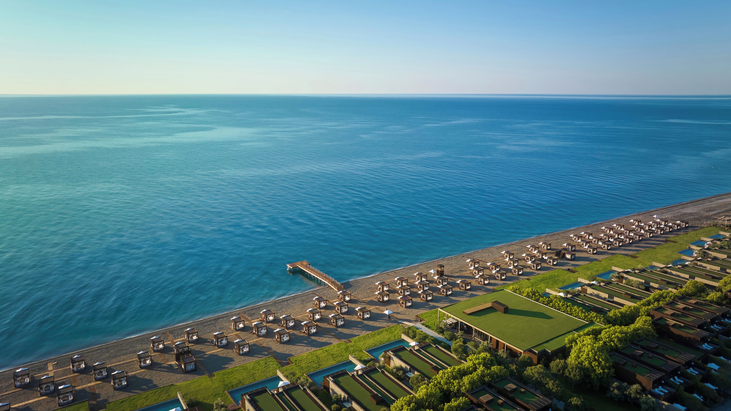 An aerial view of a coastal resort with a long beachfront, multiple bungalow-style accommodations, a central pool, and a pier extending into the sea.