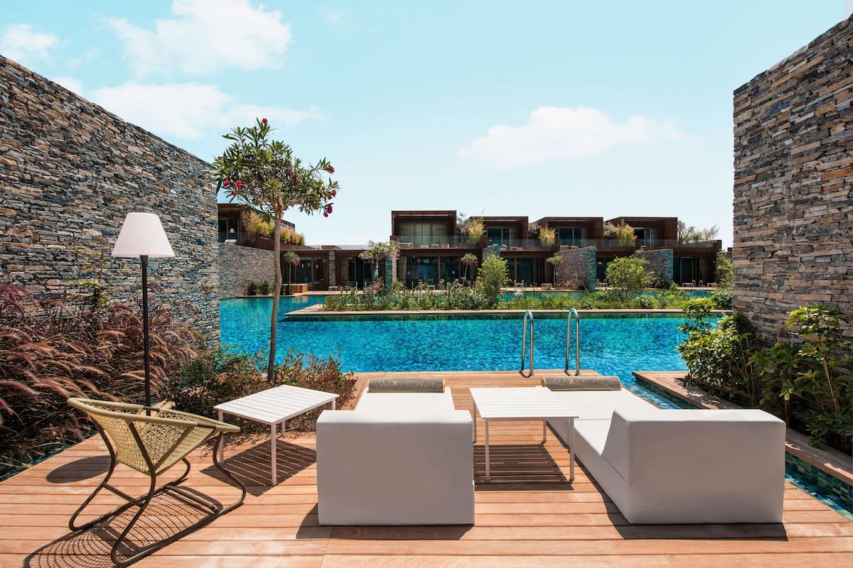 A poolside area with lounge chairs, a lamp, and a view of a modern building with a stone facade.