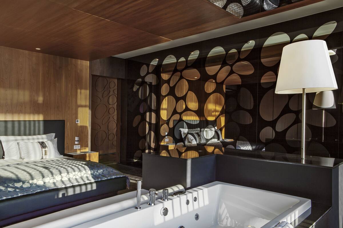 A modern hotel room with a large bed, a separate bathroom with a bathtub, and a decorative wall with circular patterns.