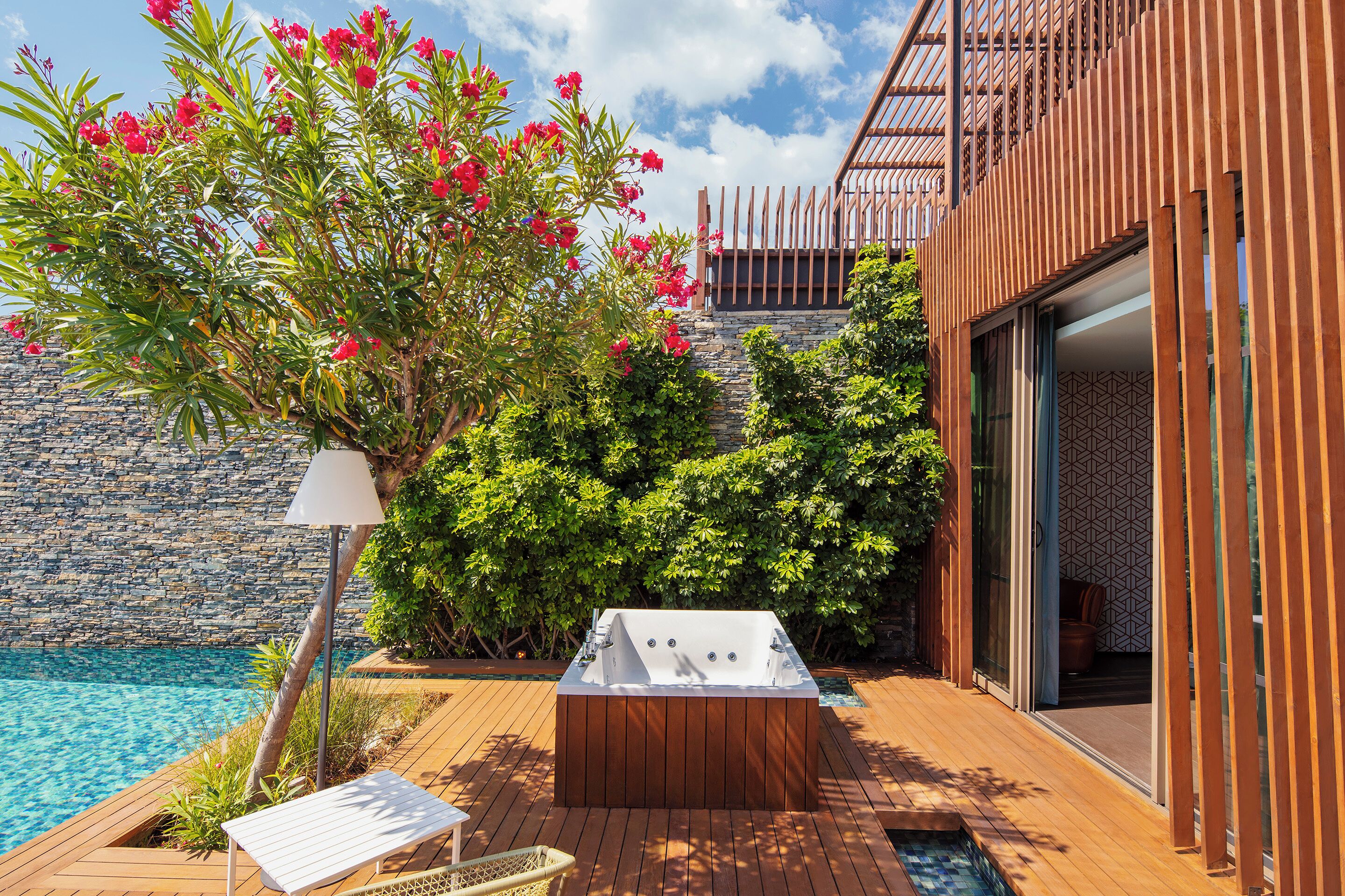 A wooden deck with a hot tub, a pool, and lush greenery.