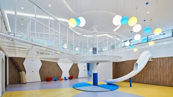 A modern indoor play area with a slide, colorful hanging lights, and a netted play structure.