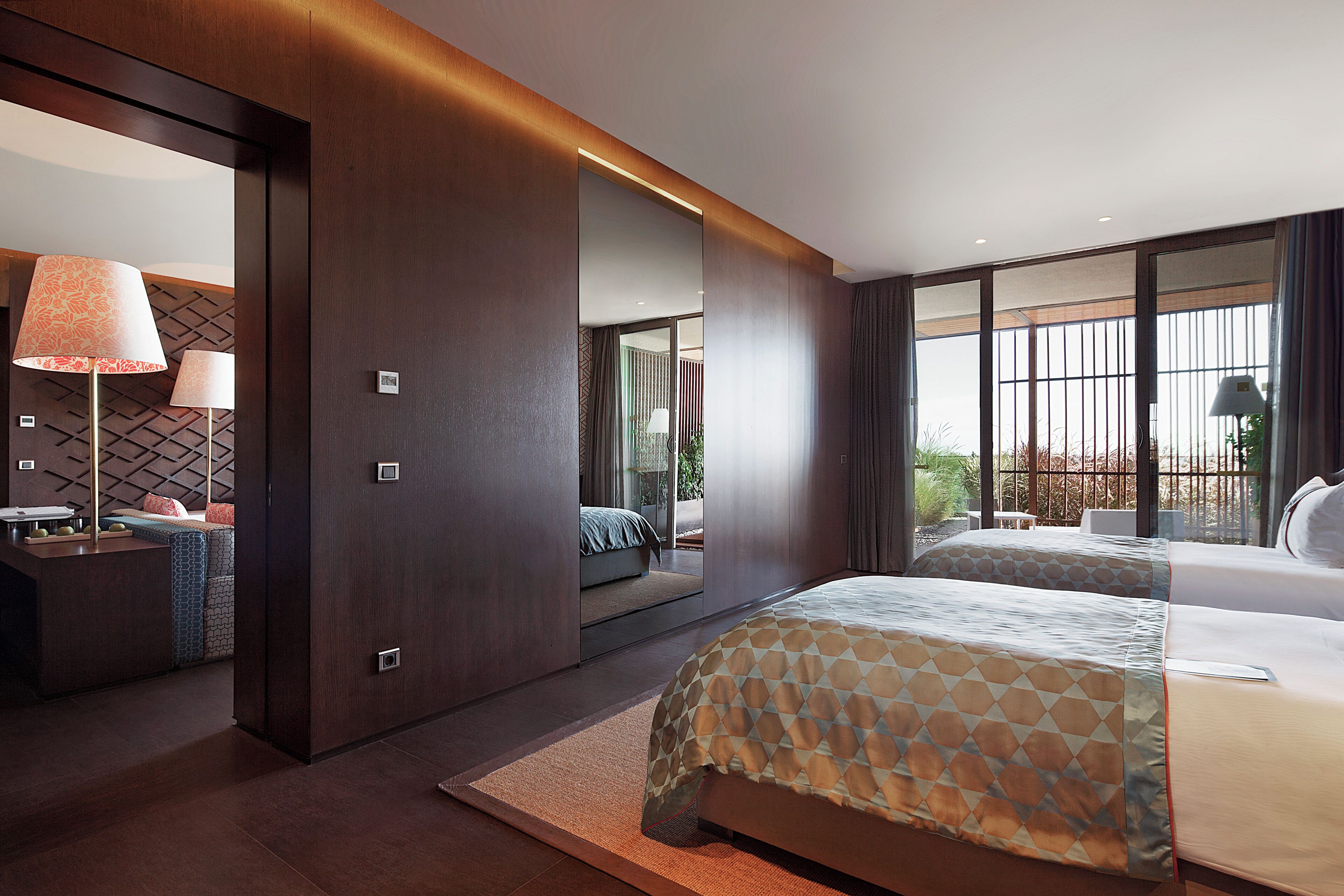 Una habitación de hotel moderna con una cama grande, una zona de estar con sofá y mesa, y un ventanal que ofrece vistas al exterior.