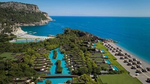 Vista aérea de un complejo turístico con múltiples piscinas, una zona de playa y abundante vegetación.