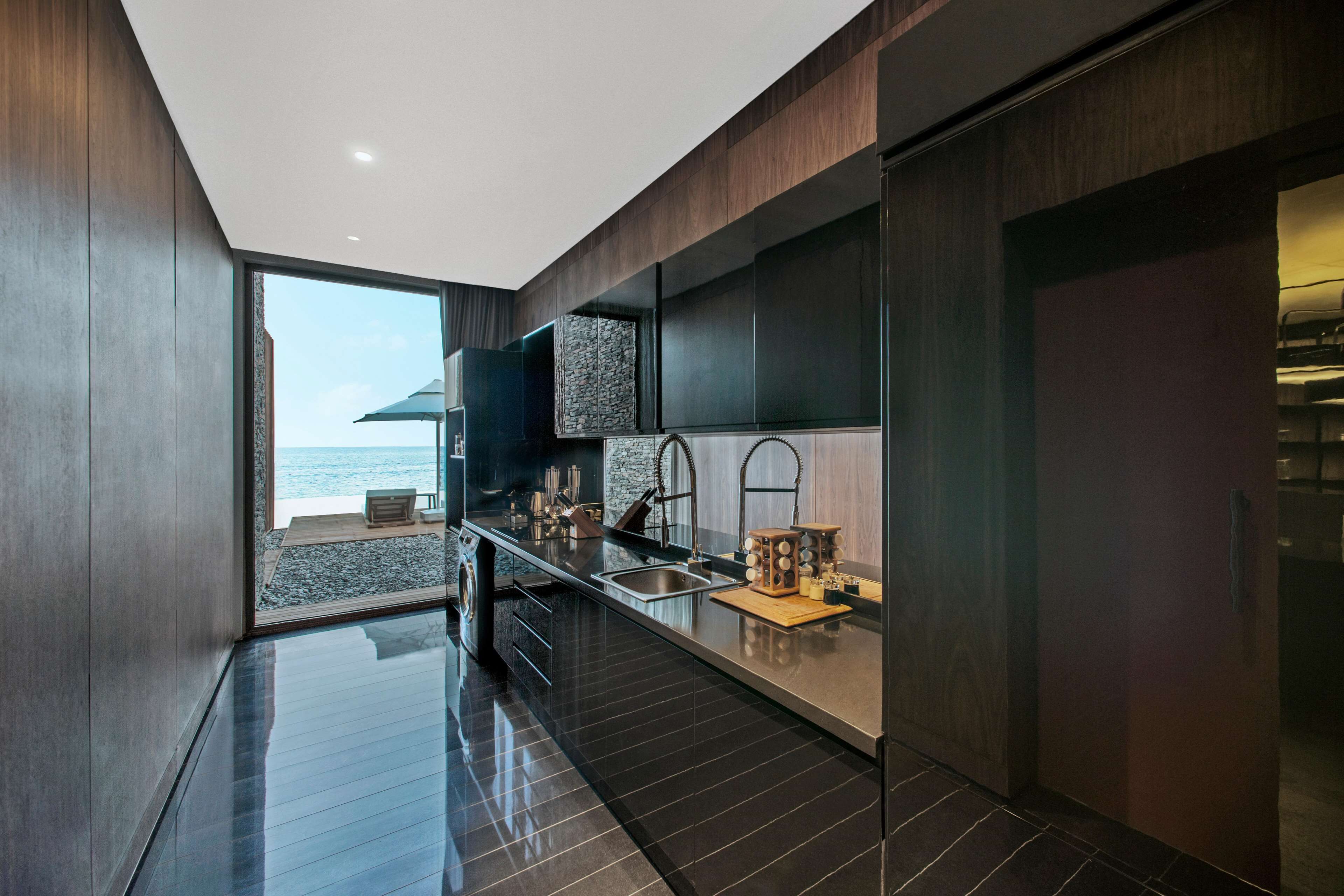 Una cocina moderna con un ventanal grande, armarios de madera oscura y vista al océano.