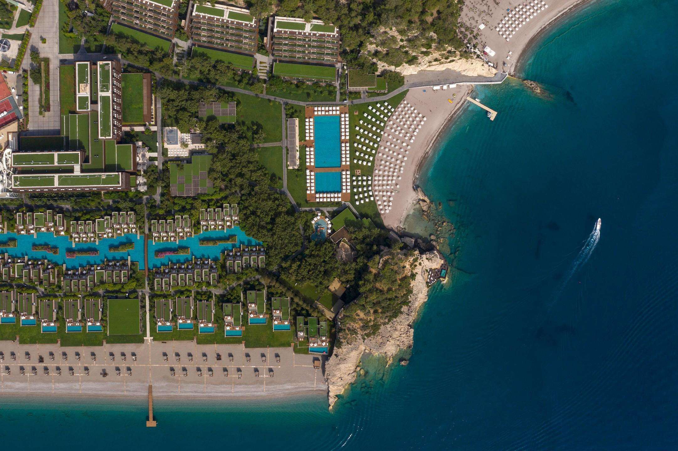 An aerial view of a coastal resort with multiple hotel buildings, a central swimming pool, and a beach area.