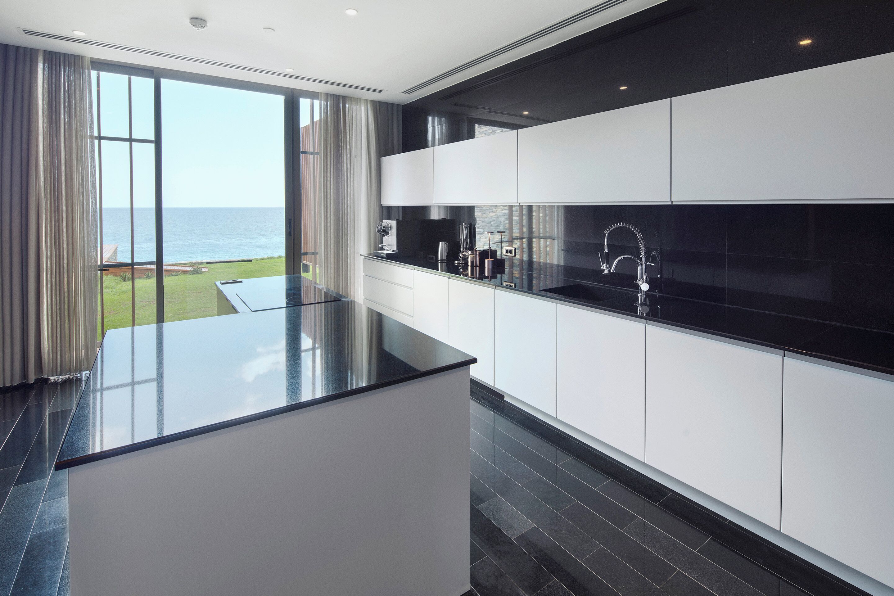 A modern kitchen with a large island, white cabinets, and a black countertop.