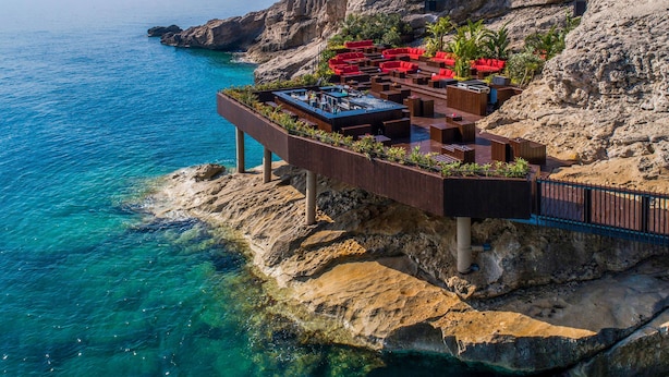 Un bar al borde de un acantilado con terraza al aire libre y vistas al mar.