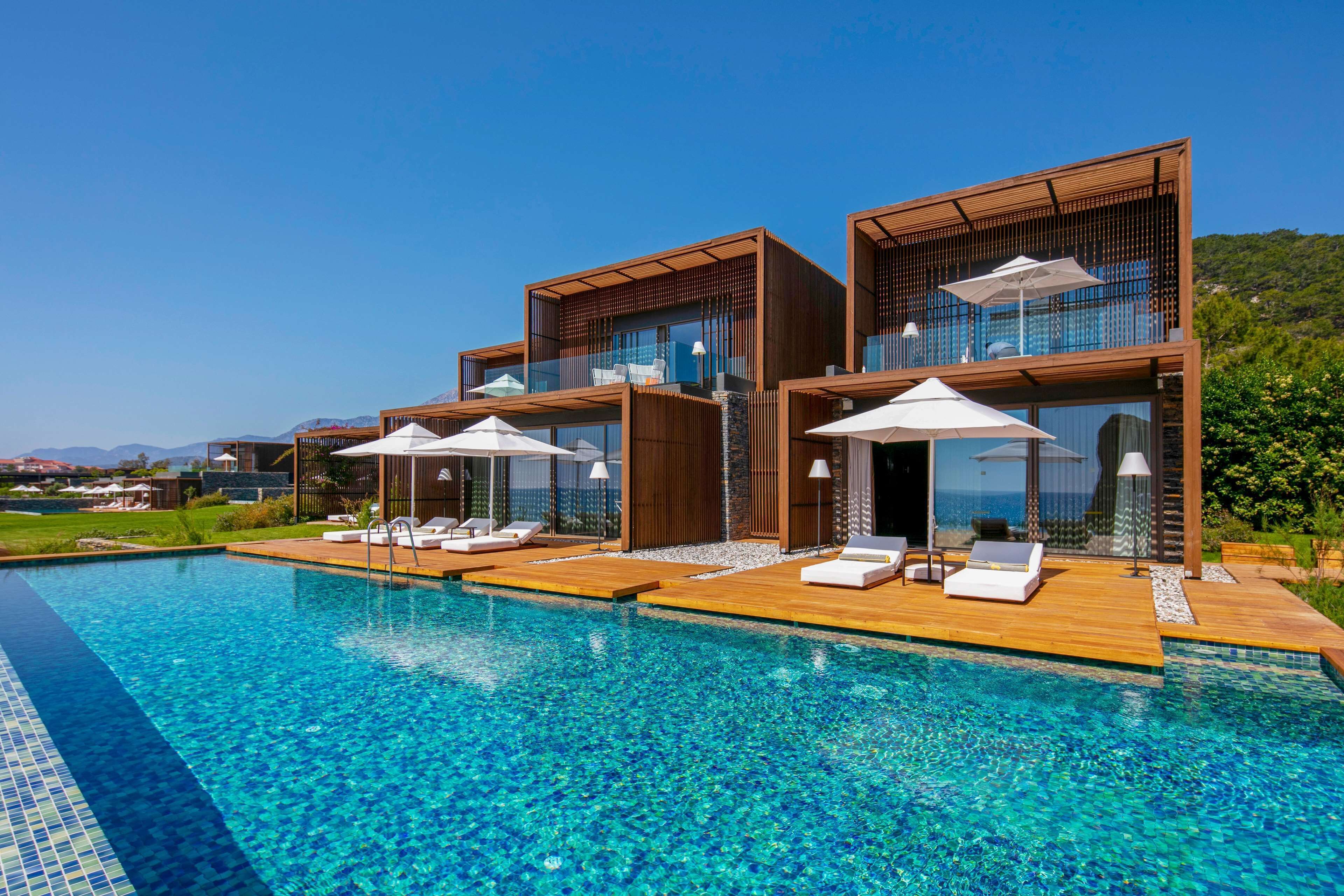 Un resort moderno con piscina, terraza de madera y sillones de descanso.