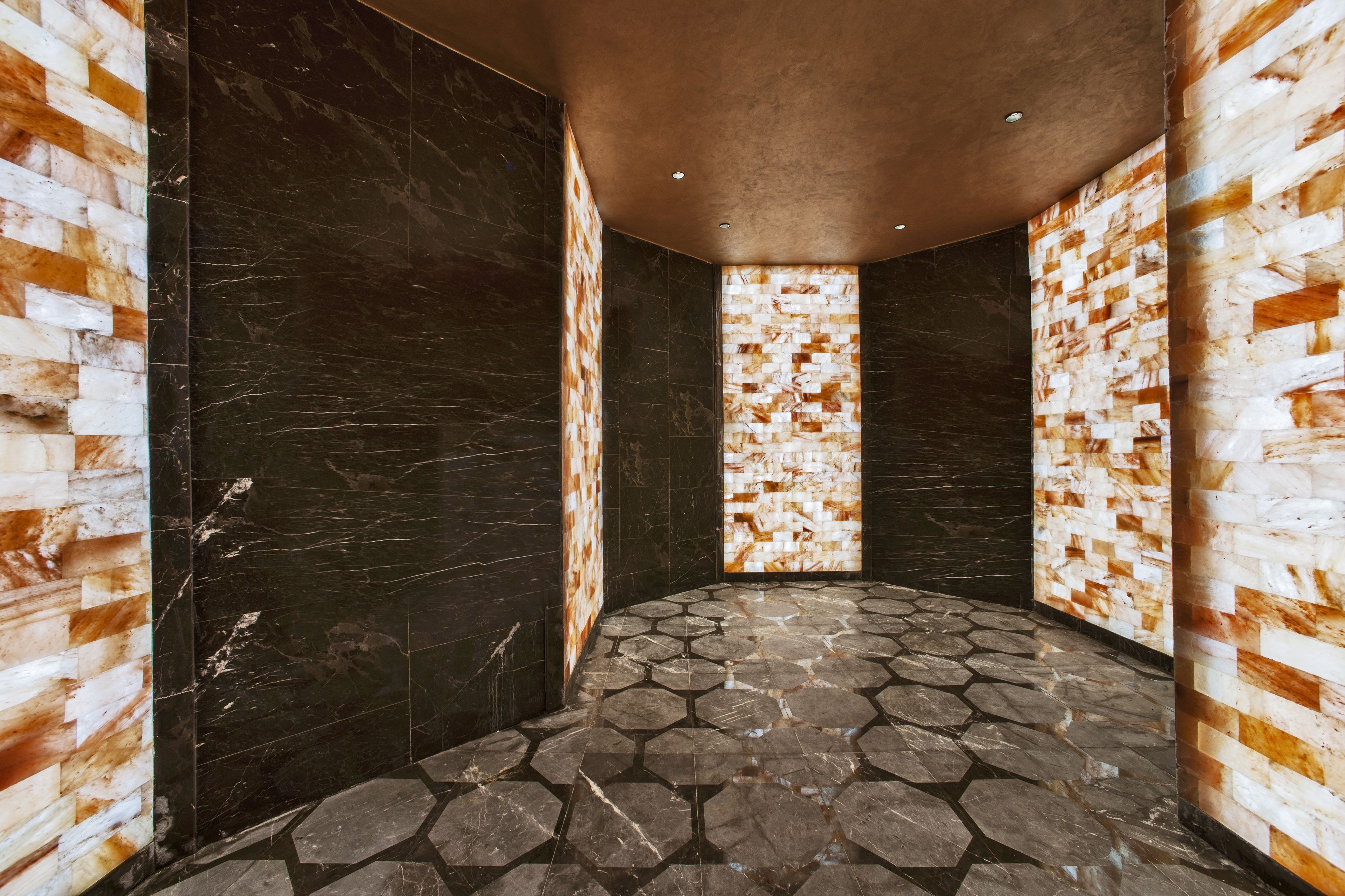 A room with hexagonal stone flooring, dark marble walls, and a textured wall panel.
