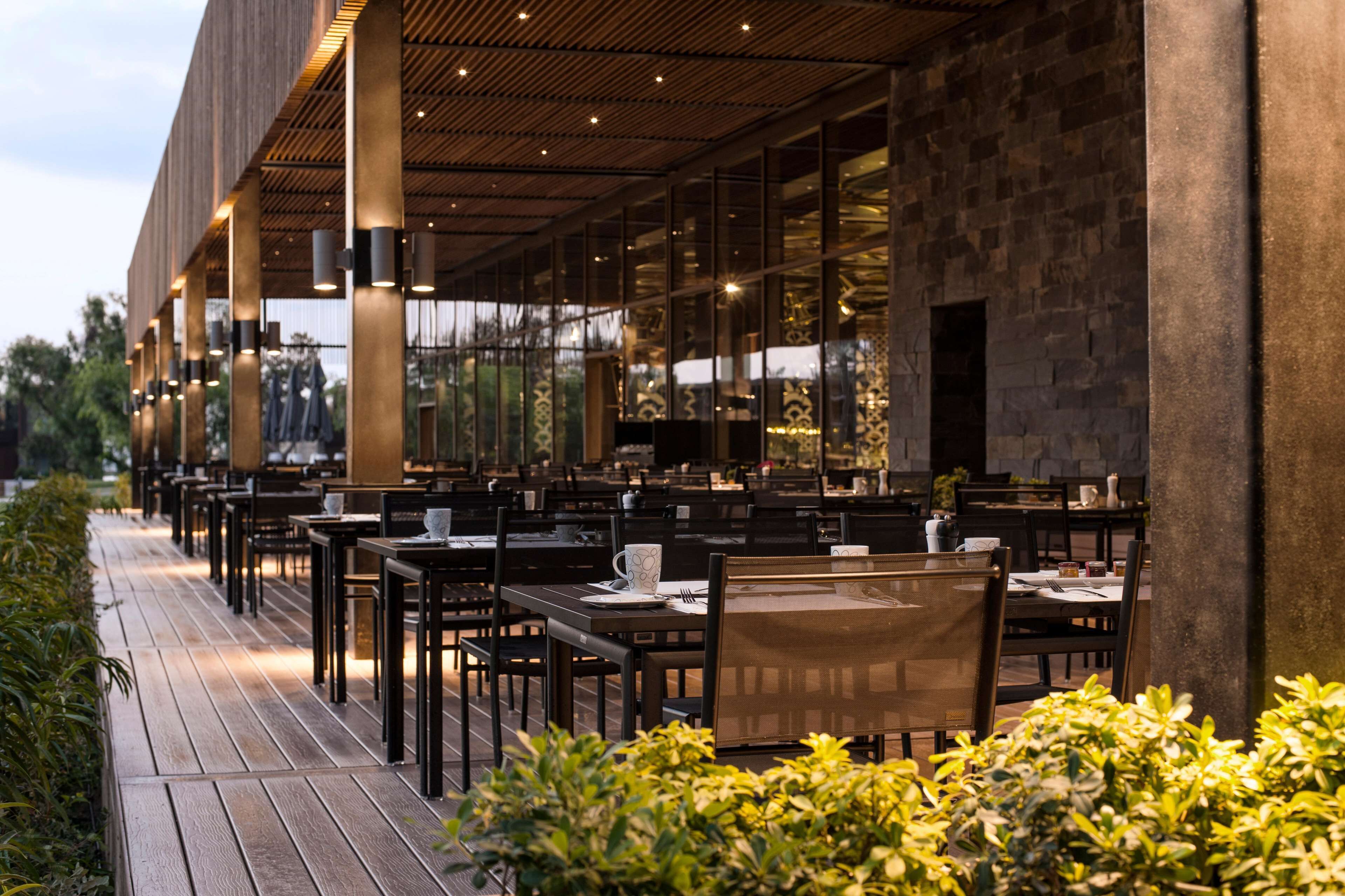 Un área de comedor al aire libre con mesas y sillas, una terraza de madera y un muro de piedra.