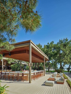 An outdoor seating area with wooden tables and chairs, a covered pavilion, and a view of the sea.