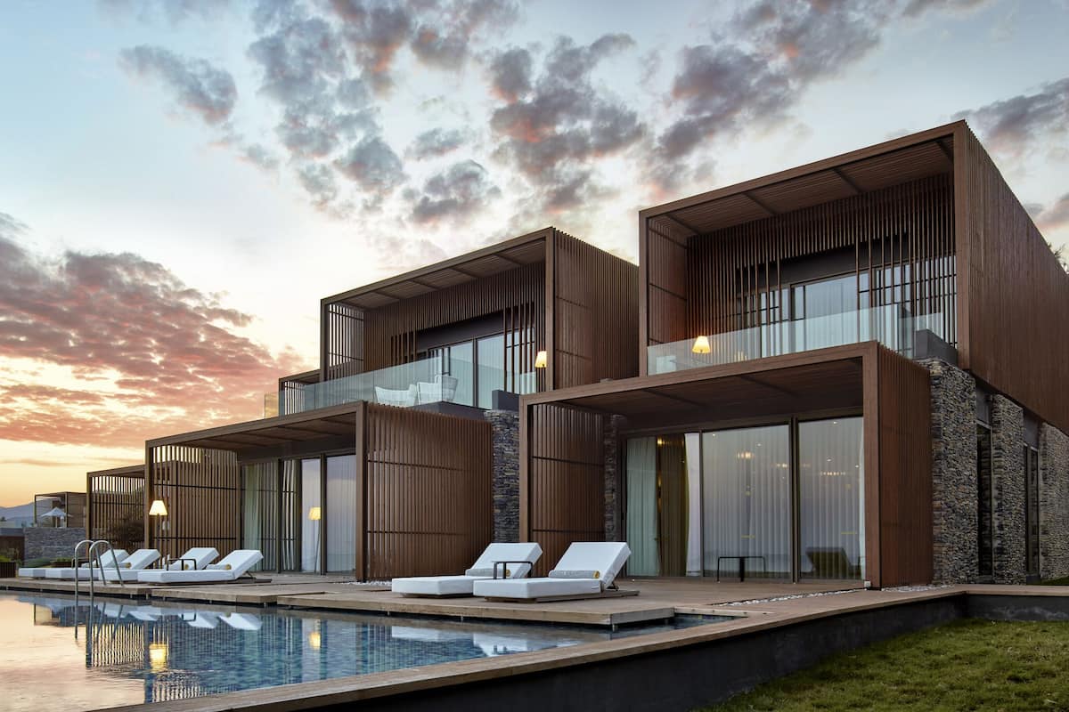A modern two-story building with a pool, lounge chairs, and a scenic sunset view.