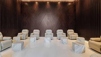 Un spa moderno con seis sillas de masaje beige dispuestas en dos filas, suelo de mármol y pared de madera oscura con diseño en zigzag.