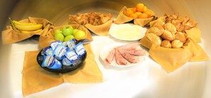 Een tafel met diverse etenswaren, zoals bananen, appels, sinaasappels, gebak en verpakte snacks.
