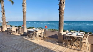 A wooden deck with tables and chairs, palm trees, and a view of the ocean. - Voyage Sorgun (Manavgat)