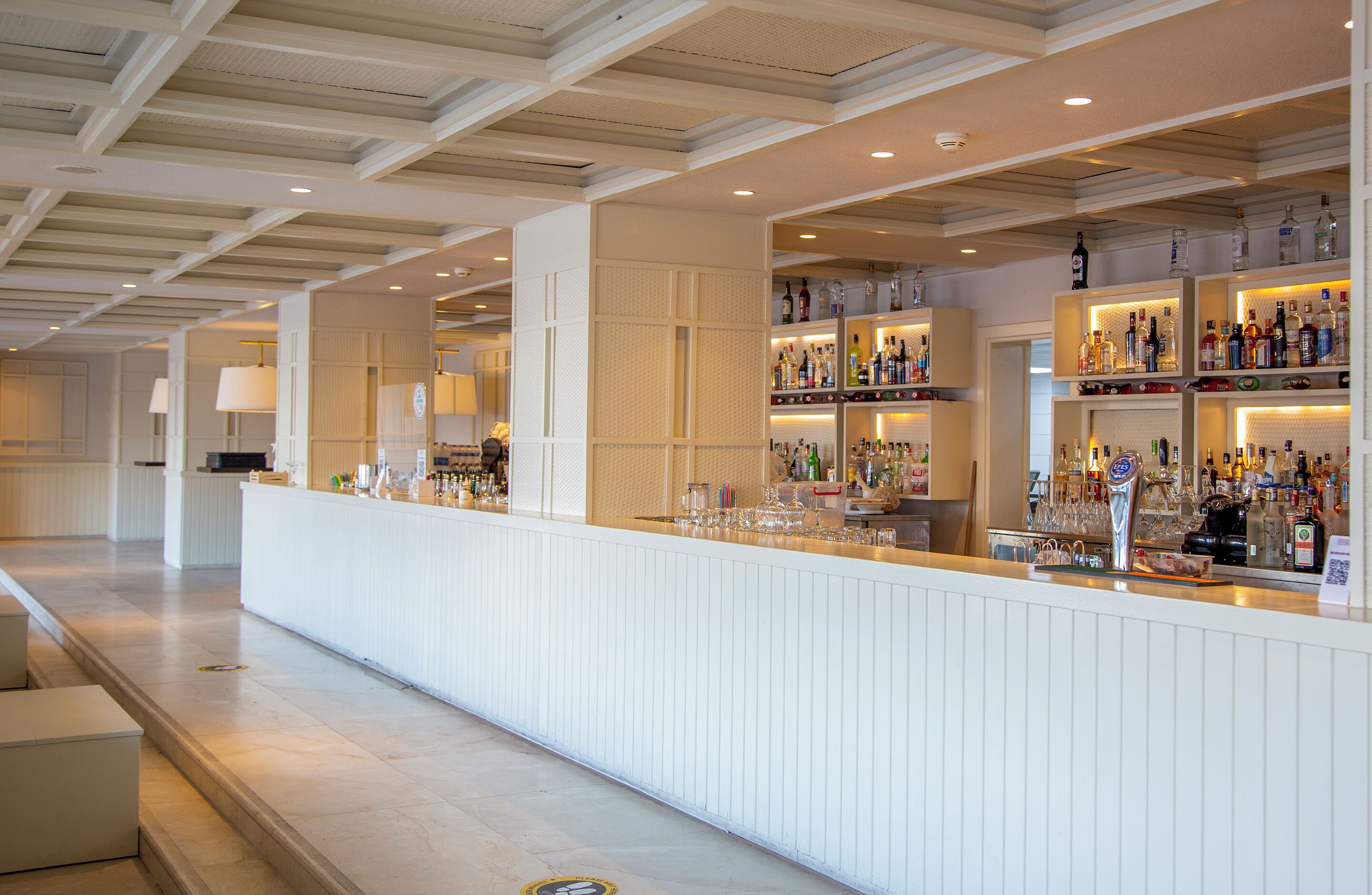 Eine Bar mit einer langen Theke, Regalen voller Flaschen und einer Decke mit freiliegenden Balken.