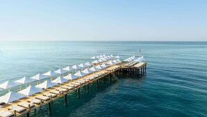 A pier with rows of white umbrellas and lounge chairs extending into the sea. - Voyage Sorgun (Manavgat)