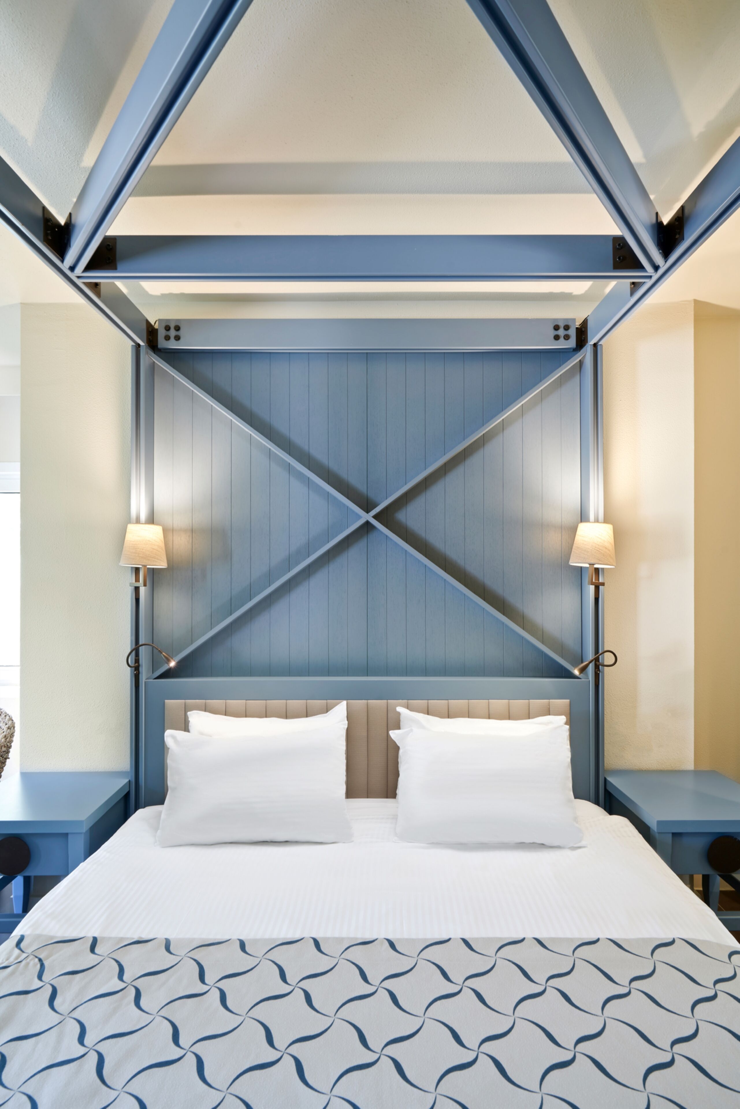 A bed with a geometric headboard, two bedside lamps, and a patterned bedspread.