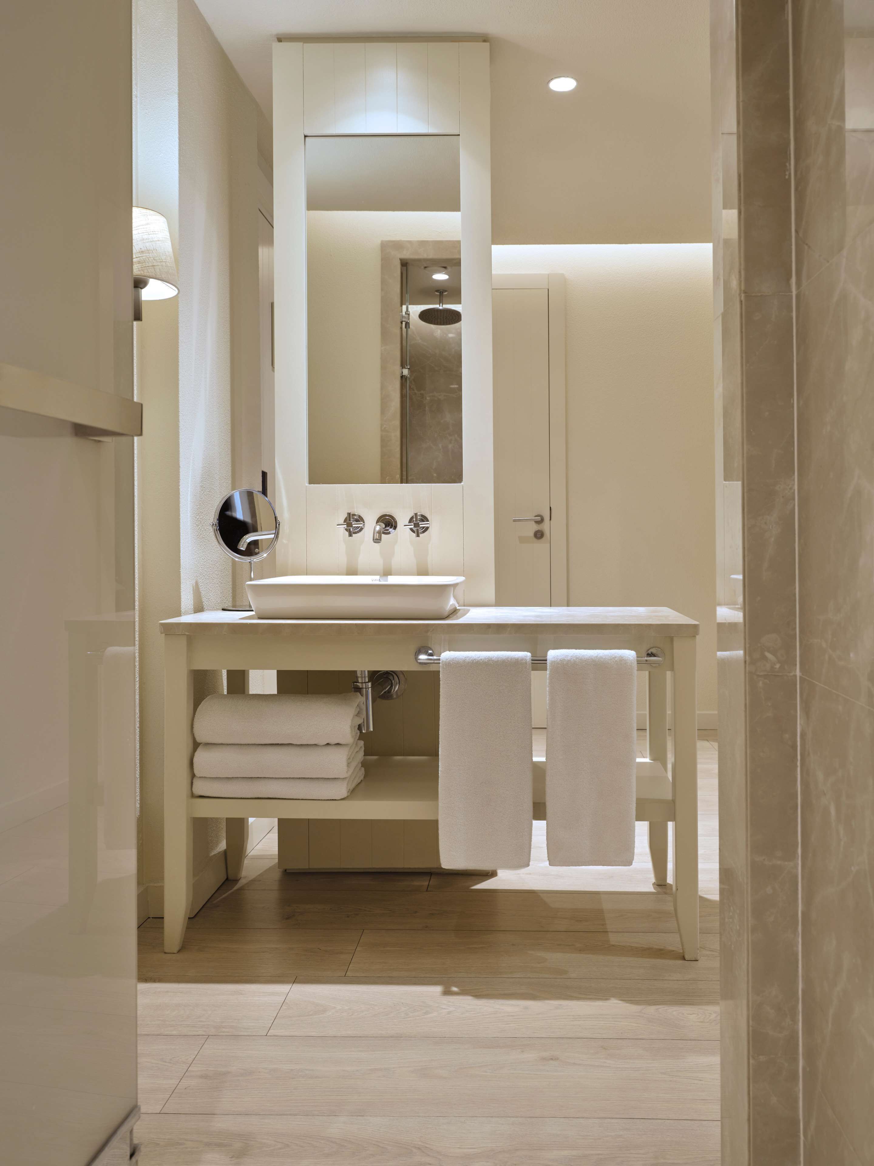 A modern bathroom with a large mirror, a sink, and two towels hanging on the wall.
