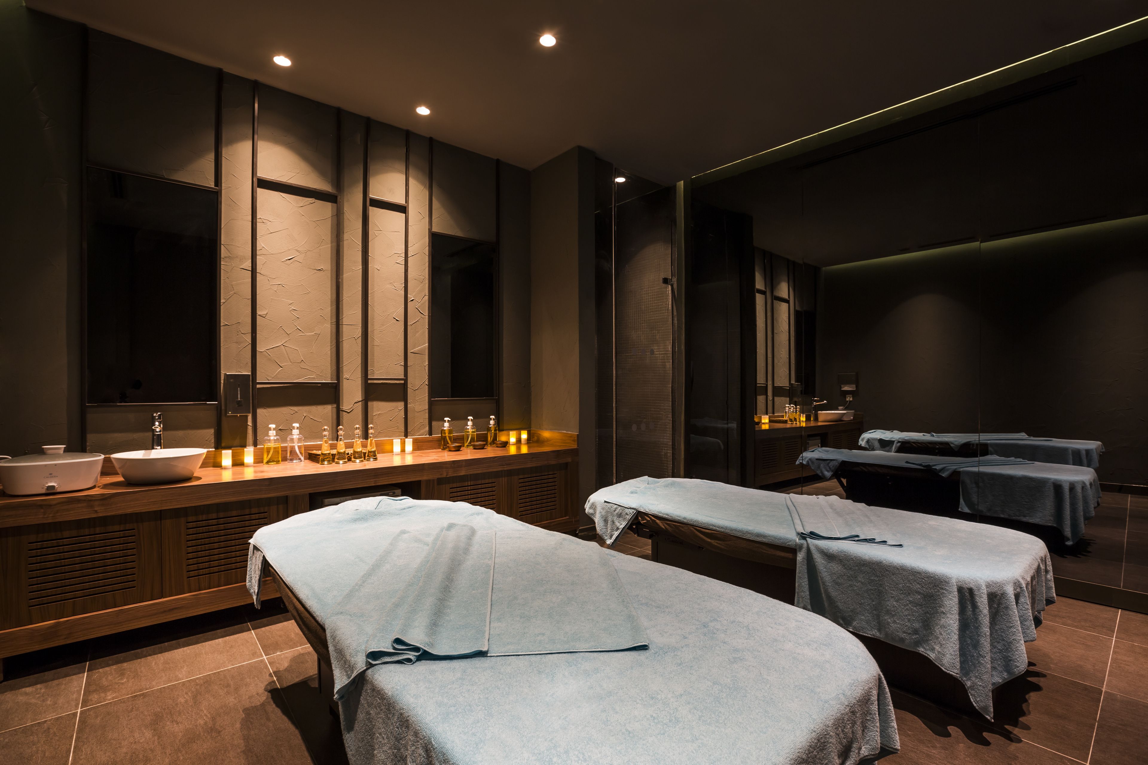 A modern spa room with a large mirror, a sink, and two massage tables.