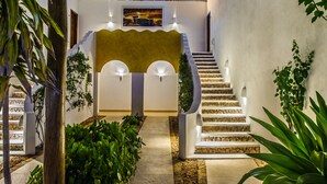 Una escalera conduce a una habitación con un muro amarillo decorativo, rodeada de vegetación y un tejado de paja.