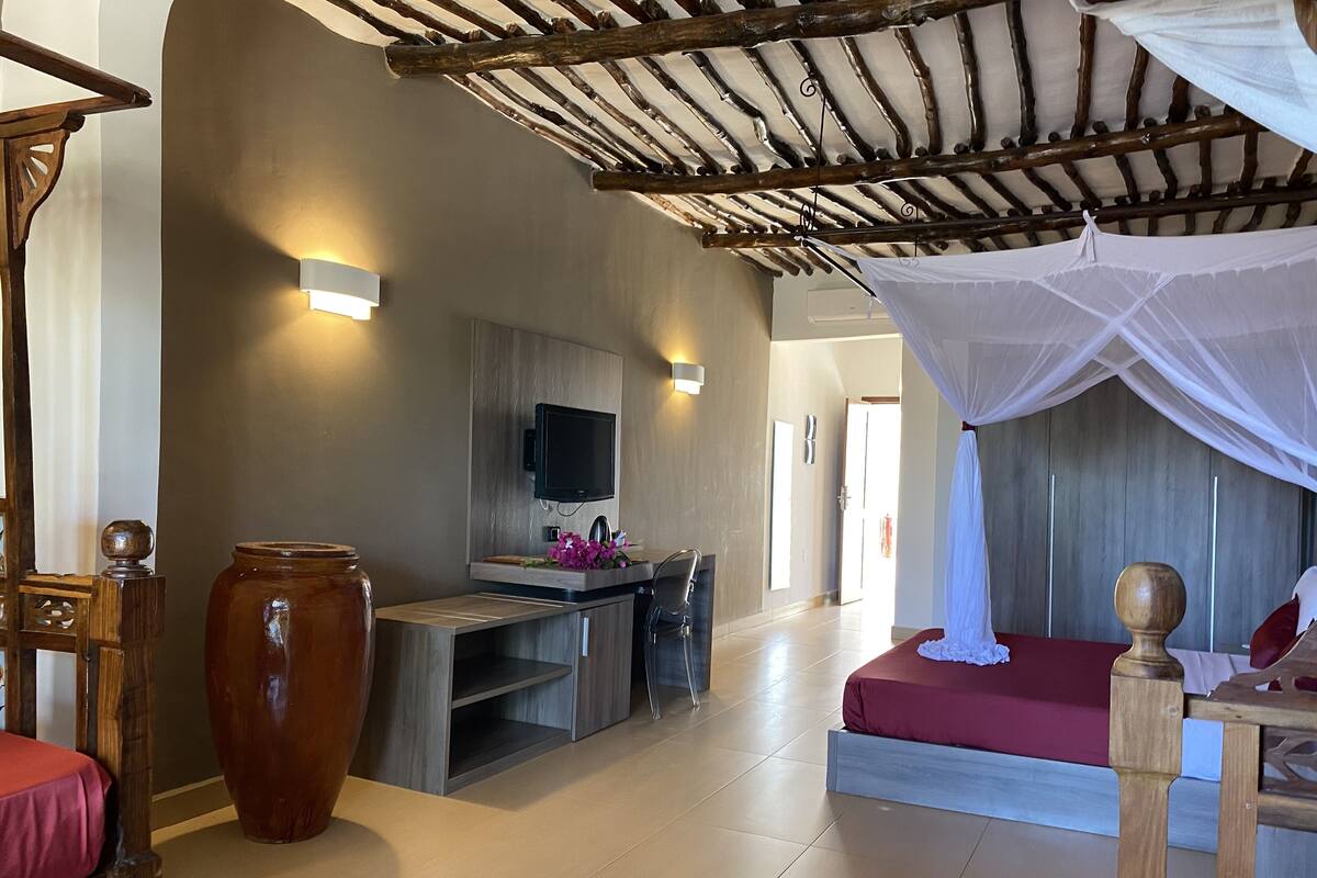 A modern room with a TV mounted on the wall, a large wooden table, a red sofa, and a canopy bed.