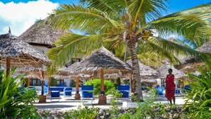 Un resort con estructuras de techo de paja, palmeras y sillones azules para lounge.