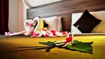 A neatly made bed with a heart-shaped pillow and a single rose on the bedspread.