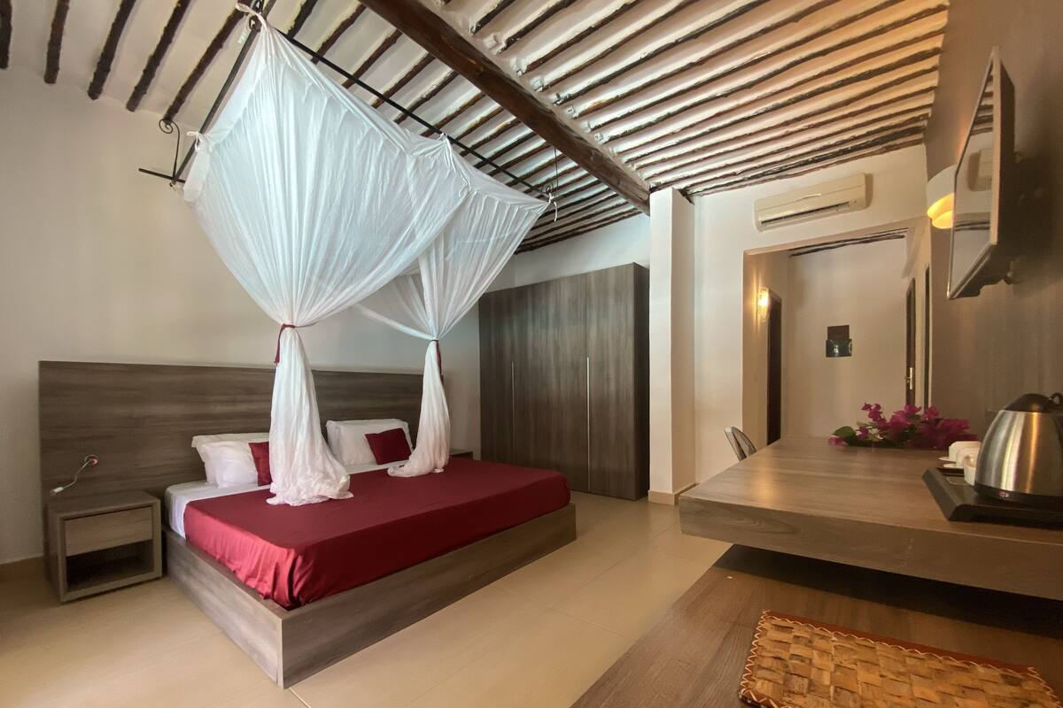 A bedroom with a bed, nightstand, wooden headboard, and a ceiling with wooden beams.