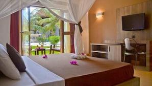 Habitación de hotel con cama, escritorio, silla, televisión y vista a palmeras.
