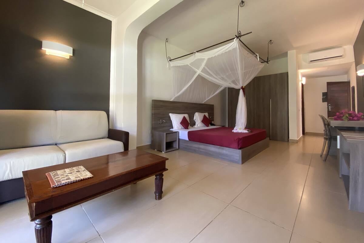 A modern hotel room with a bed, a sofa, a coffee table, and a dining area.
