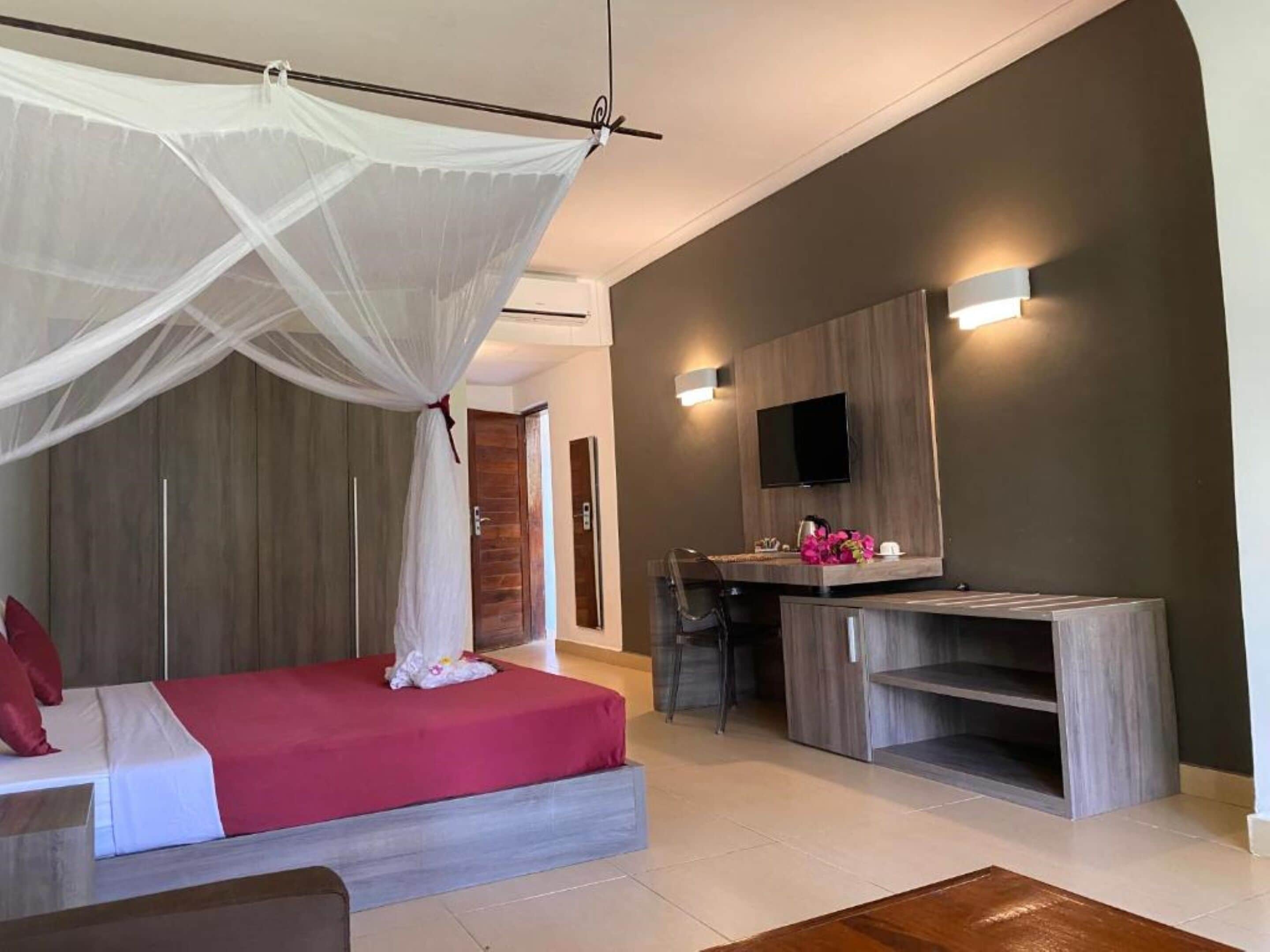 A modern bedroom with a canopy bed, a TV mounted on the wall, and a small kitchenette area.