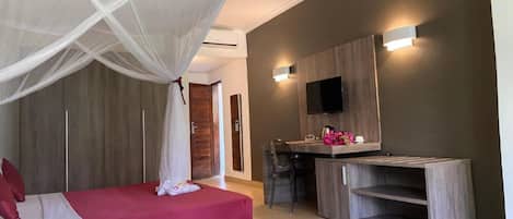 Un dormitorio moderno con cama con dosel, televisor montado en la pared y una pequeña área de kitchenette.