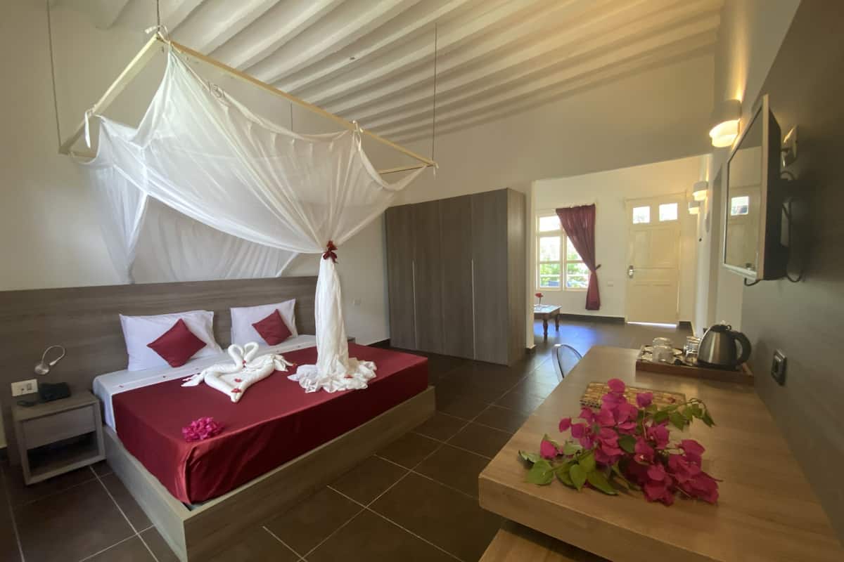 A hotel room with a bed, a nightstand, a wooden table with flowers, a mirror, and a view of the outside.