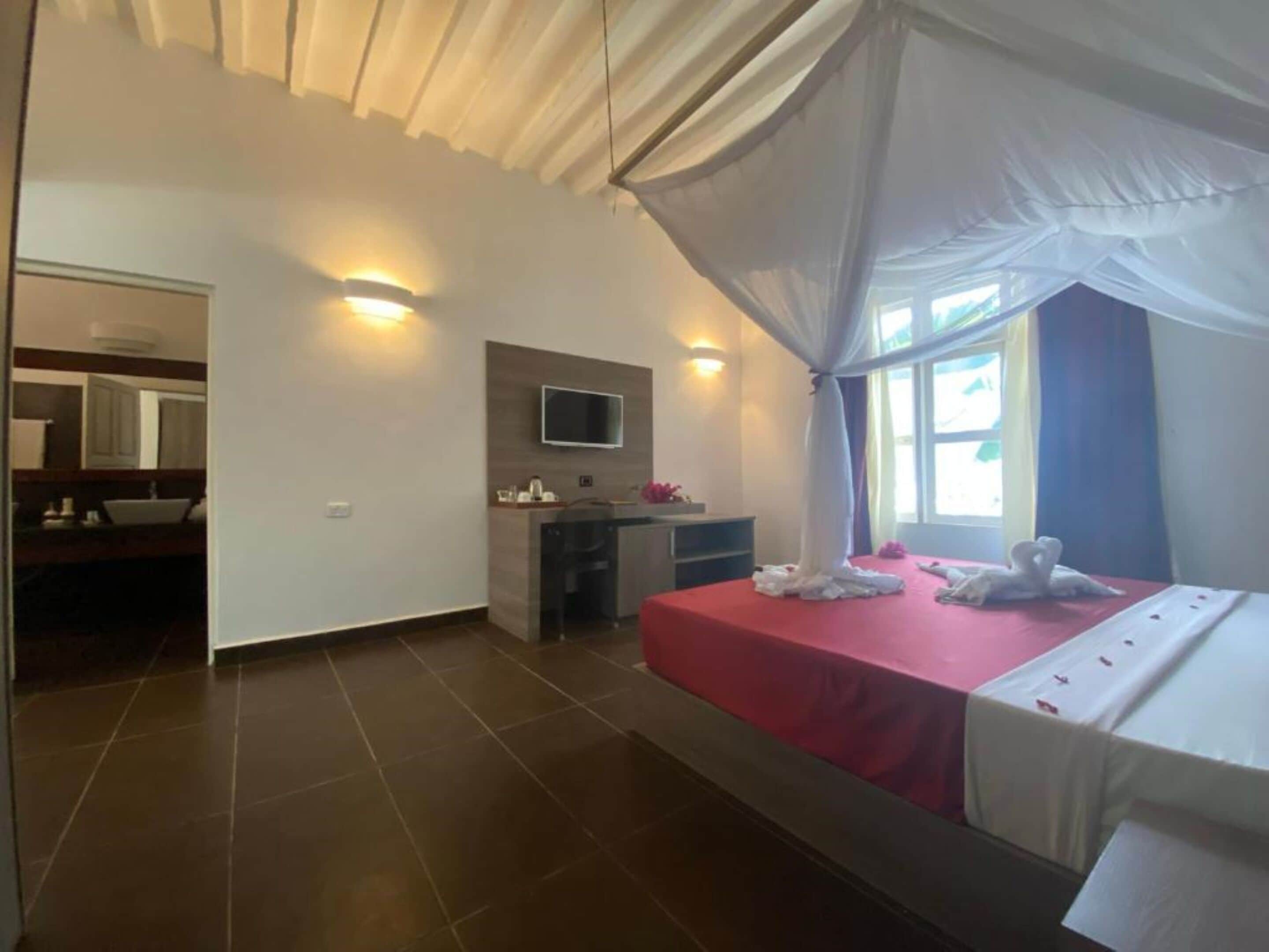 Een hotelkamer met een bed, een televisie, een klein bureau en een badkamer die door een open deur zichtbaar is.