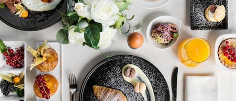 A table set with various dishes including eggs, pastries, and fruit, arranged on a tablecloth with a vase of flowers.