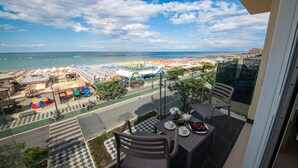 Un balcón con una mesa lista para comer, con vista a una playa con sombrillas y un parque infantil.