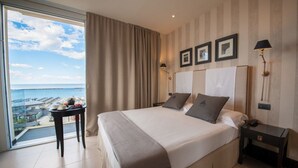 Habitación de hotel con una cama grande, una mesita de noche, una mesa con vistas y un balcón que ofrece vistas al mar.