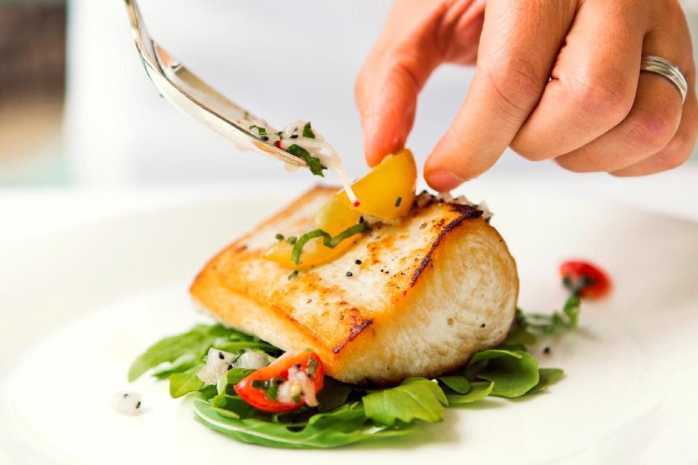 A hand placing a lemon wedge on a piece of grilled fish on a plate.