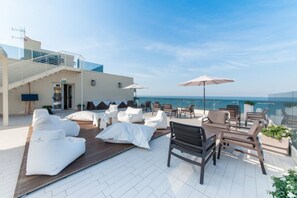 A rooftop terrace with white lounge chairs, a wooden table, and umbrellas, overlooking a clear blue sea. - Vista Mare Hotel (Cesenatico)