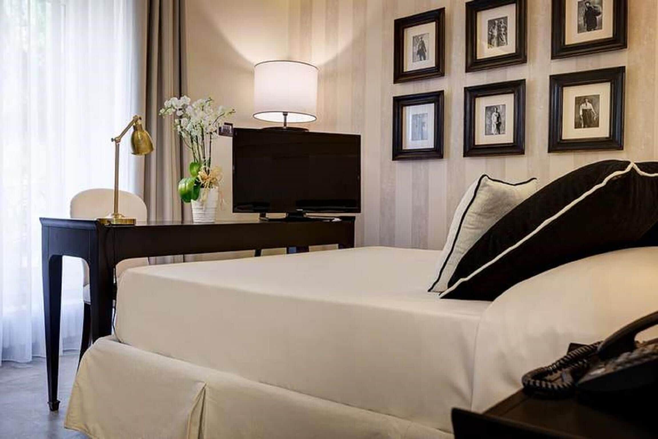 Habitación de hotel con cama, escritorio con lámpara, televisor y cuadros en la pared.