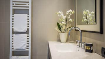 Ein modernes Badezimmer mit einem weißen Handtuchhalter, einem Waschbecken mit Spiegel und einer Vase mit weißen Blumen.