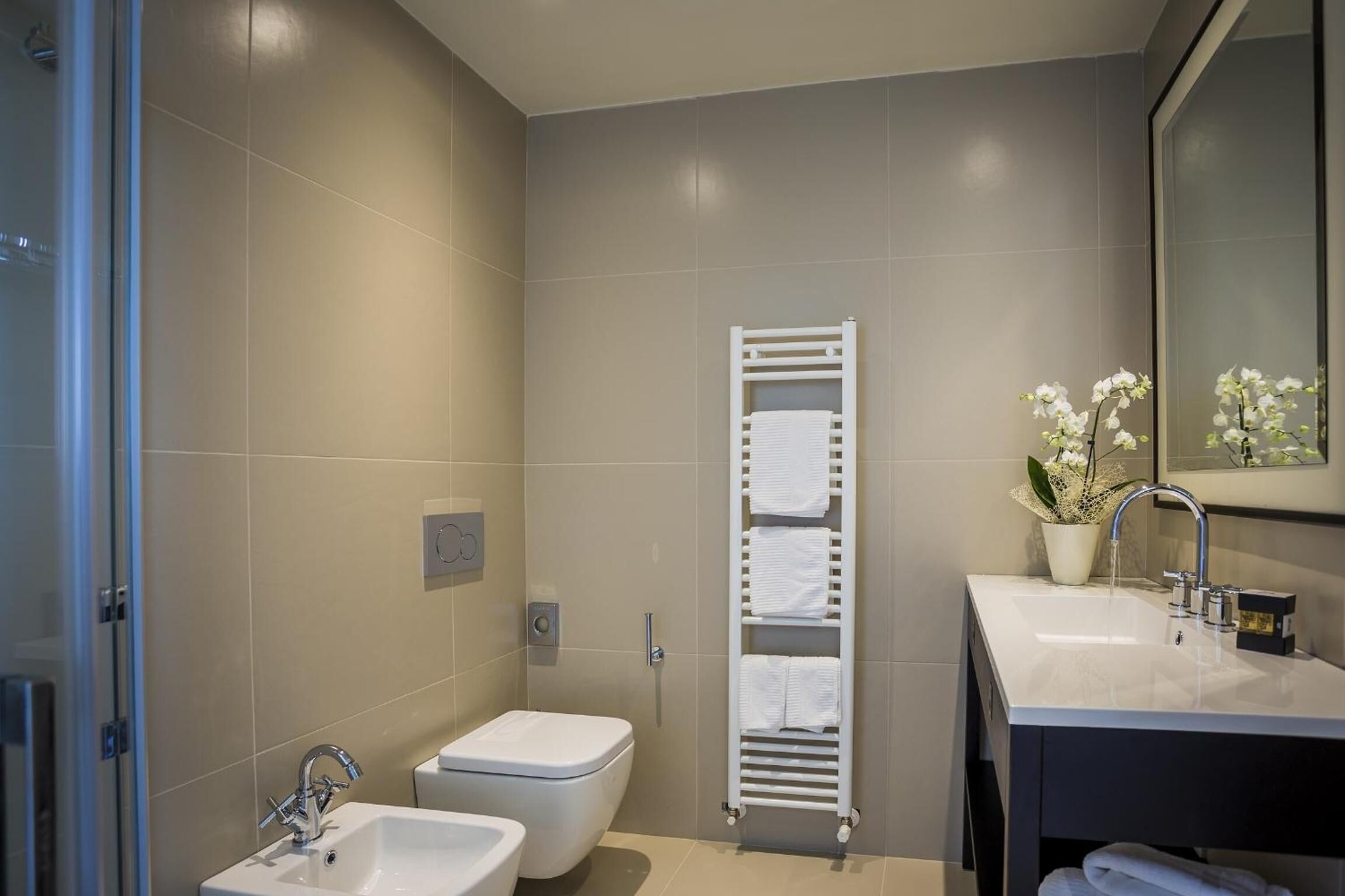 A modern bathroom with a toilet, bidet, sink, and towel rack.