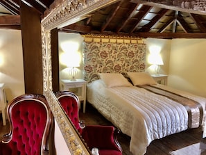 A bedroom with a large bed, two bedside tables, a mirror, and a red chair.