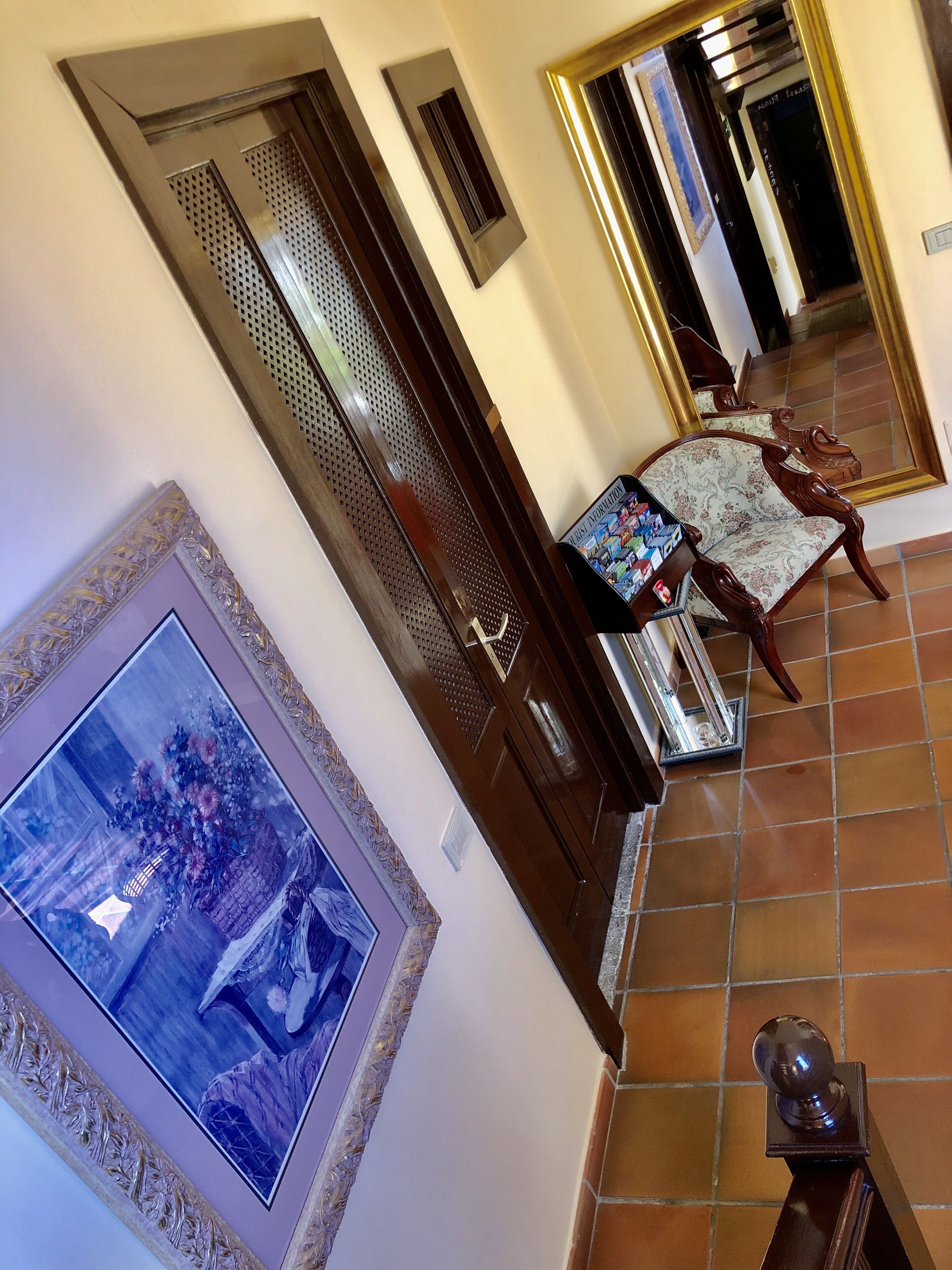 A room with a large mirror, a chair with a floral pattern, and a framed picture on the wall.