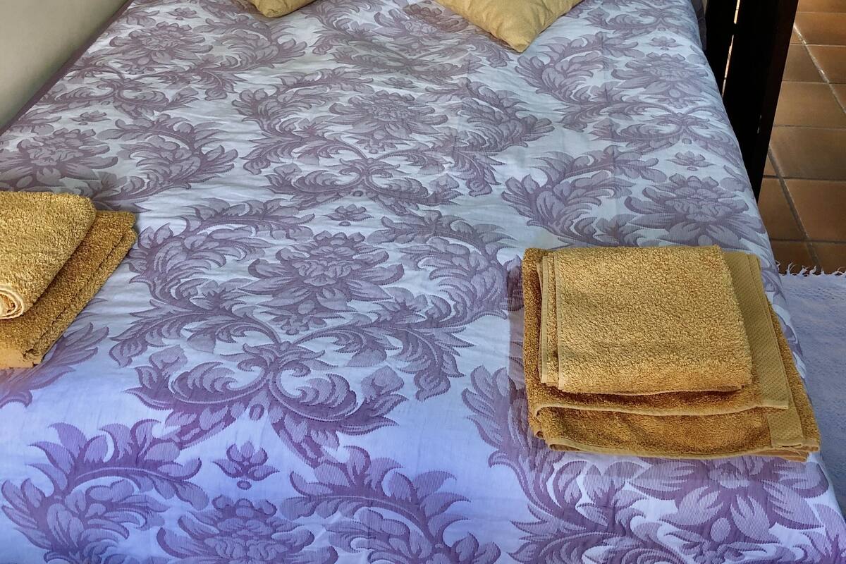 A bed with a floral-patterned bedspread, two beige pillows, and two folded towels on the bed.