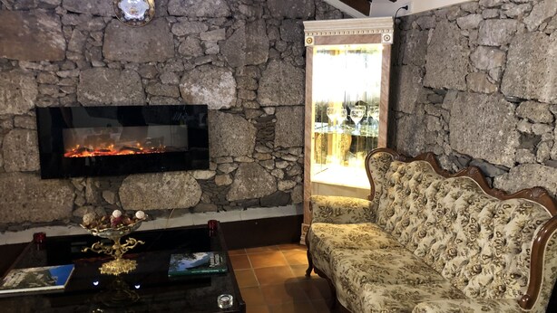 A room with a stone wall, a fireplace, a sofa, and a table with a vase and book. - Hotel Rural Vilaflor (Vilaflor)