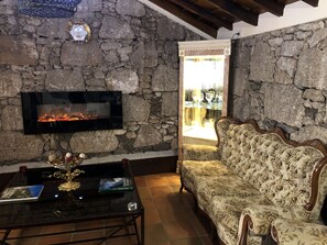 A room with a stone wall, a fireplace, a sofa, and a table with a vase and book. - Hotel Rural Vilaflor (Vilaflor)